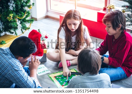group of children or kids are learning and playing crossword board game in living room with Christmas tree and gift boxes background