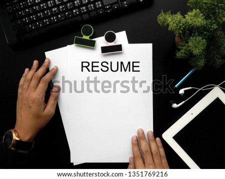 Resume paper white on black work desk with tablet, glasses, plant , earphone , pen ,keyboard and hand man on top view