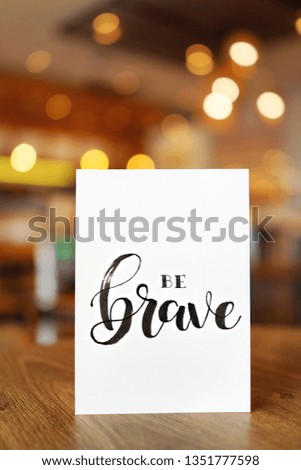 Inspired motivation quote "Be Brave" with blurred cafe interior as background                                 