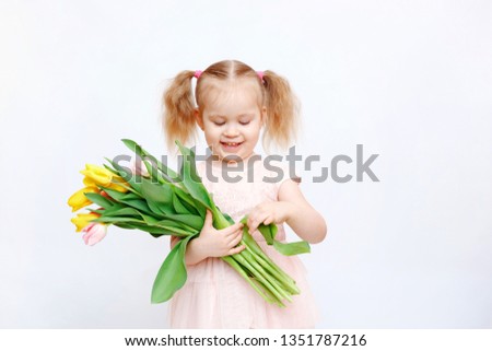 Little beautiful girl blonde with a bouquet of tulips on a light background. Baby girl smiling. Spring and women's day concept. Little girl holding a bouquet of colored tulips. Сopy spase