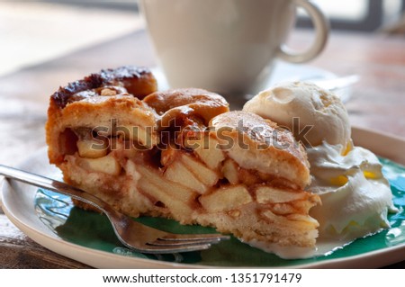 Warm apple pie tart with scoop of vanilla ice cream on whipped cream with cappuccino in the background 