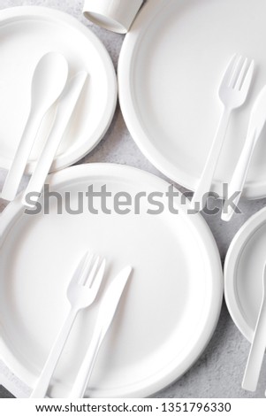 set of empty reusable disposable eco-friendly plates, cups, utensils on light white and grey concrete table top with copy space. Top view. 