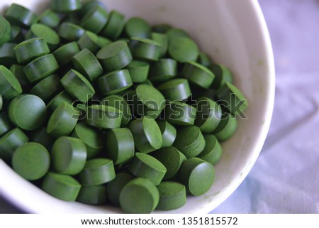 spirulina and chlorella  tablets on the light background. green tablets in the small bawl