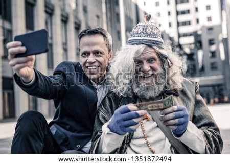 Crazy businessman photographing. Desperate poor old man kissing dollar bill while smiling man making photo of the process