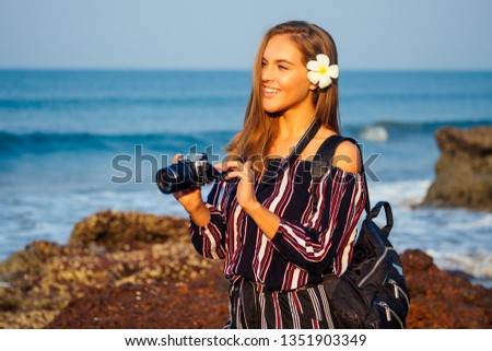 tropical enjoyment summertime tourism and photography. Young traveling woman in a stylish striped jumpsuit with camera and backpack near sea beach indian ocean goa turquoise water, sky and rocks