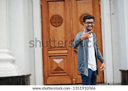Stylish indian man at glasses wear casual posed outdoor against door of building, show rock fingers sign.