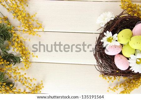 Easter eggs in nest and mimosa flowers, on white wooden background