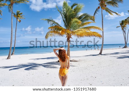 Model in a yellow swimsuit on the sand palm tropics blue sea                    