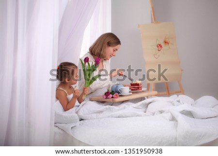 Breakfast in bed for mother in Mother`s Day. Bouquet of tulips presented to mom in morning. Mother tastes cake in bed.