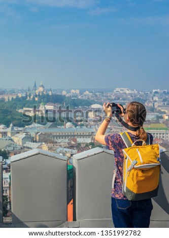 Young Girl Tourist Photographer with a Yellow Backpack Takes Pictures of Sights. Travel Concept. Panorama of the Old Town