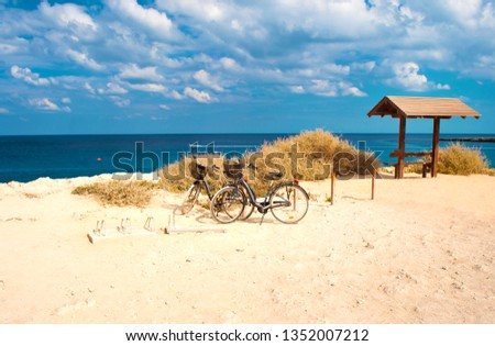 Two bicycles with baskets parked against deep blue azure water near Cape Greco, Cyprus. Dramatic cloudy sky, amazing seascape. Warm and sunny day in fall. Concept of wanderlust and adventure