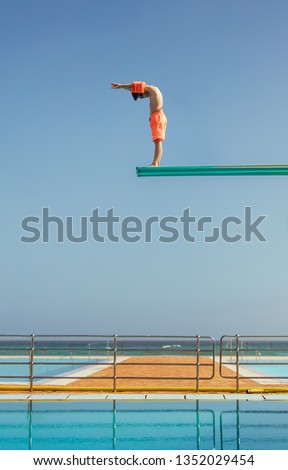 Boy stands on a diving platform about to dive into the swimming pool. Boy standing on high diving spring board preparing to dive. Royalty-Free Stock Photo #1352029454