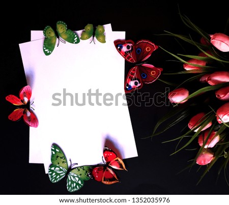 black background with a white sheet in the center, pink tulips and six beautiful butterflies of green and pink colors
