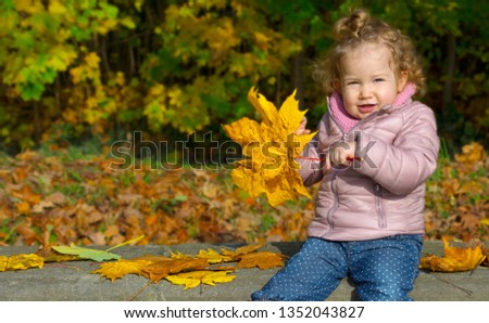 Toddler is sitting outside on a bench in the park in autumn