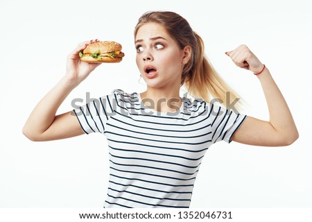 A woman striped t-shirts with a hamburger in her hands looks surprised in the light background