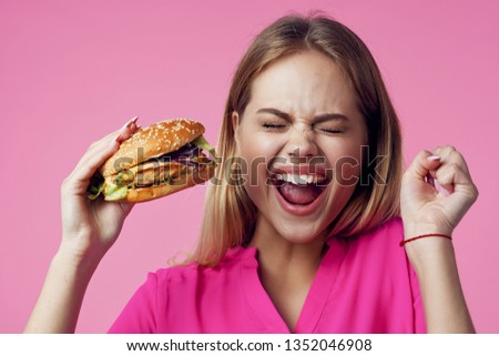 pretty woman with a hamburger in the hands of pink background fast food model