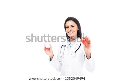 Doctor in white coat with stethoscope holding pills and plastic heart isolated on white