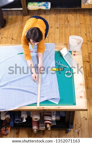 High angle view of female seller of fabric shop measuring and cutting off piece of textile for dressmaking 