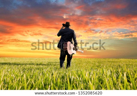 the american cowboy with his classic guitar at the countryside of texas on a sunset evening