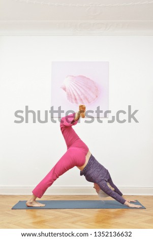 Senior woman exercising yoga at home on a mat in front of a wall with a shell picture, asana tripod