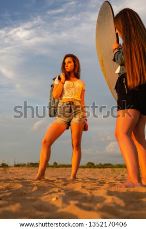 A woman holds a reflector at a photo shoot. Sunset. Bright orange sun. Lady posing at camera with the reflector. 