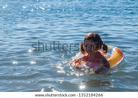 Little cute girl in lifebuoy inflatable circle in the sea. A child learns to swim with joy. Safe swimming training. Picture for a family holiday with children on the sea. Beach holiday with children.