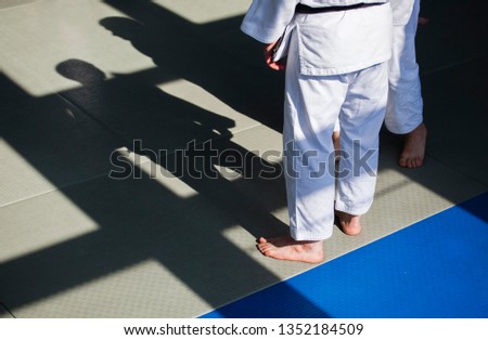 A trainer with a white kimono stands on the tatami, watching the workout. His shadow falls before him