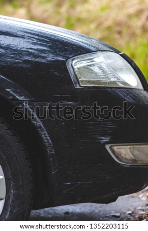 Front of a black car. White scratches on the black fender car of the Automobile. Car side view. Headlight, wheel, bumper. Vertical photo