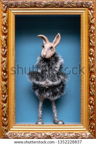 A doll rabbit in a fur coat in a picture frame