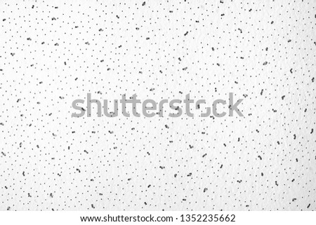 Abstract gray-white background with black dots and specks. The empty light surface of a gypsum-cortona ceiling sheet with small holes. 