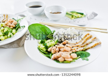 Spring menu of Asian restaurant, bowl with glass noodles, beans, chicken breast, spinach, arugula and cucumber. White background, side view, space for text