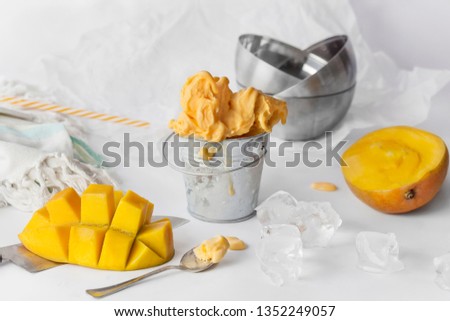 Mango ice cream in a metal mini bucket decorated with sliced mango cubes on white background