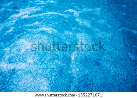 Summer abstract background of Outdoor water splash in Jacuzzi or whirlpool for massage & spa at exotic tropical resort hotel, copy space. Fresh water bubbles & white waves on swimming pool surface Royalty-Free Stock Photo #1352271071