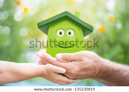Family holding eco cartoon house in hands against green spring background. Environment protection concept