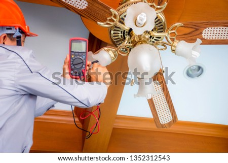 Technician man hand holding and using multimeter to checking  voltage at the electrical terminal of the light lamp at the ceiling fan. Replace or changing lamp at home. Maintenance concept.