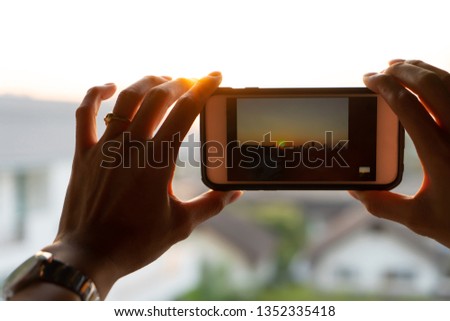 Close up woman hand holding smartphone taking photo sunset city. Beautiful scene on screen.
Girl using mobile phone take picture of silhouette building in city view from roof top.