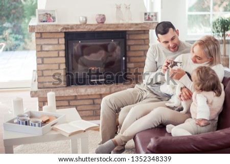 The family sits on the couch near the fireplace. Mom, Dad, daughter and cat in the home interior.