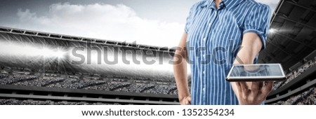 Mid-section of woman holding a tablet against composite image of sport arena