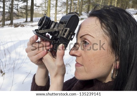 woman using vintage camera in snow covered woodland