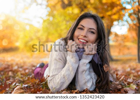 Portrait of an attractive woman lying in colourful autumn leaves in a park during the folden season in october