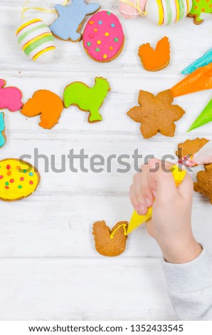 Child hands decorating honemade gingerbread with icing sugar using a pipping bag. Easter Treats. Handmade cookies, standing on the table. series of step by step photos. Royalty-Free Stock Photo #1352433545