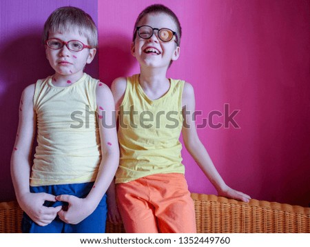 Two brothers of boy in yellow T-shirts and glasses. Children sit on sofa on pink background. Kids are happy together.