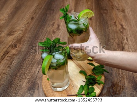 female hand holds a glass with a mojito drink, mojito with mint, ice and lime on a wooden table background, macro photography