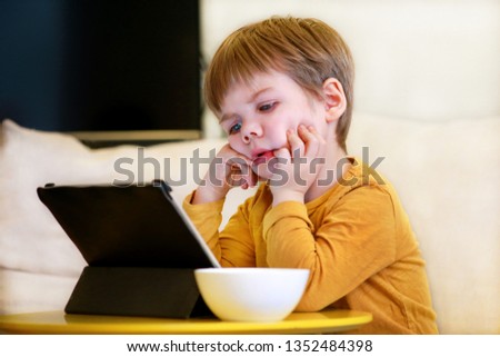Child using tablet pc on bed at home. Cute boy on sofa is watching cartoon, playing games and learning from laptop. Education, fun, leisure, happiness, modern computer technology and communication.