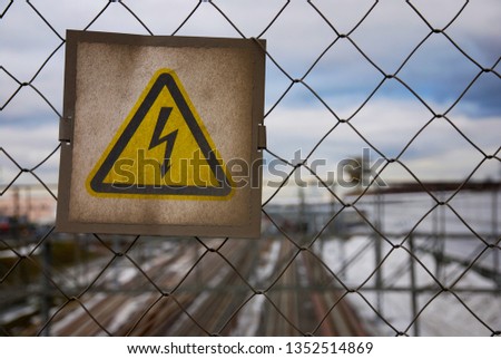 High voltage sign on the fencing net covered with dust or dirt on railway background