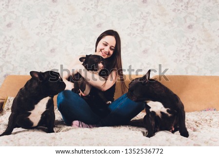 A beautiful young girl sits and holds a lot of small puppy of a French bulldog dog.