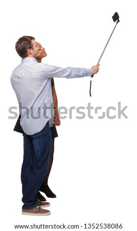 Back view of an interracial couple that makes selfie on selfie stick. beautiful friendly girl and guy together.  Isolated over white background. Young people make a photo for memory.