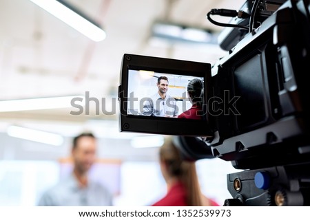 Happy businessman during corporate interview with female journalist. Manager answering question in office. Young woman at work as reporter with business man and cameraman shooting video for broadcast Royalty-Free Stock Photo #1352539973
