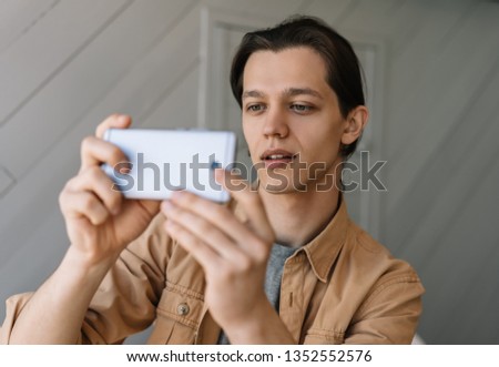 Hipster guy using smartphone, taking mobile photo. Successful blogger streaming video online. Stylish man holding modern device, watching movie on website 