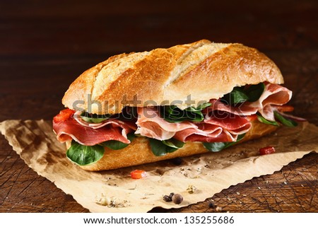 Preparing a delicious ham and fresh basil baguette on a sheet of grungy oily paper with remnants of seasoning